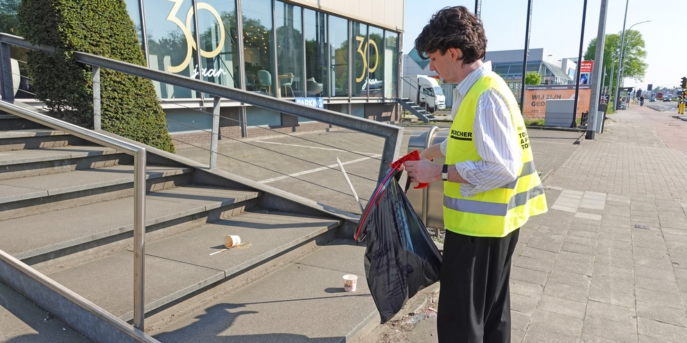 Un homme en gilet jaune Kärcher ramasse les déchets près des escaliers d'un immeuble de bureaux