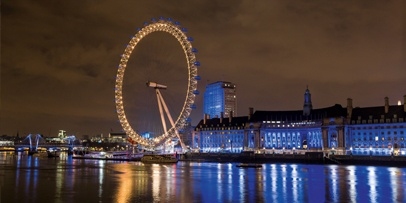 De London Eye stralend verlicht in de nacht aan de oever van de Theems De verlichte London Eye 's nachts aan de oever van de Theems.