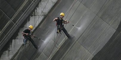 Samenwerking met GSAR voor kabeltoegangstechniek op de 56 meter hoge damwand Twee industriële klimmers hangen aan touwen en spuiten algen en mos van de betonwand van de stuwdam.
