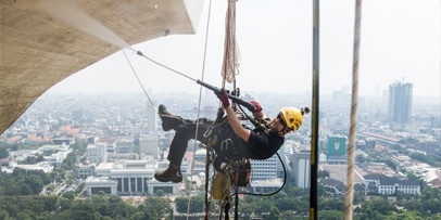 Verwijdering van roet, vet en emissieresten met de HDS 12/18-4 S warmwater-hogedrukreiniger Industriële klimmer spuit heet water op de obelisk met de stad Jakarta op de achtergrond.
