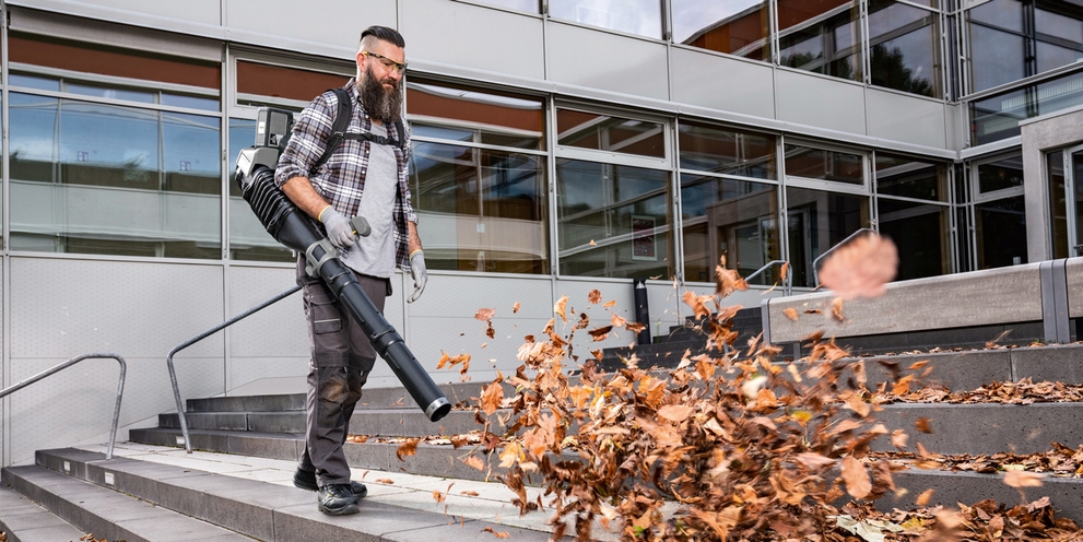Een man reinigt trappen buiten met een Kärcher bladblazer die herfstbladeren wegblaast