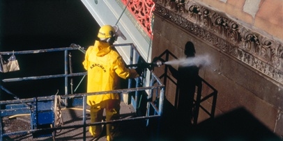 Zorgvuldige reiniging met 0,1–0,3 mm kwartszand ter bescherming van het historische materiaal uit 1888 Technicus op het platform richt de spuitlans op de versierde randen en de stenen details van de Princes Bridge.