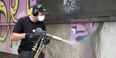 Reinigen van de betonsokkel met een lagedrukstraalpistool en toevoeging van water tegen stofontwikkeling Een Kärcher-medewerker straalt graffiti van de betonsokkel van het Brecht-Bau met aluminiumsilicaat.