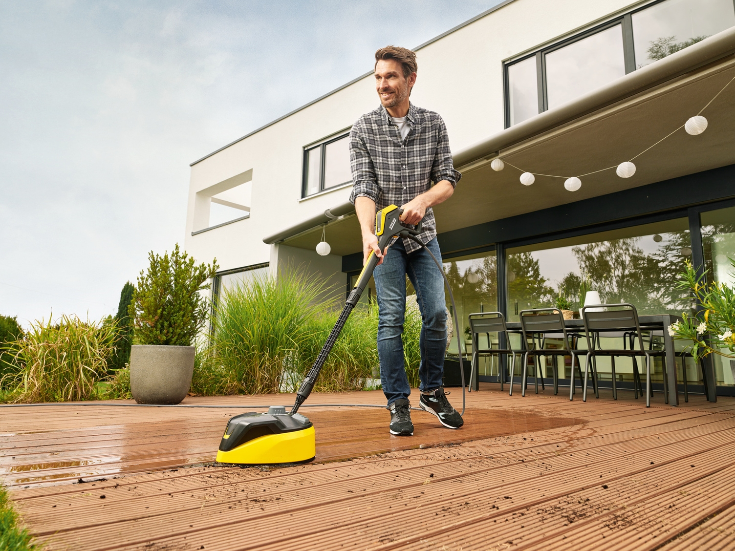 Ein Mann reinigt seine Terrassenplatten mit einem Kärcher Hochdruckreiniger mit Flächreiniger-Aufsatz
