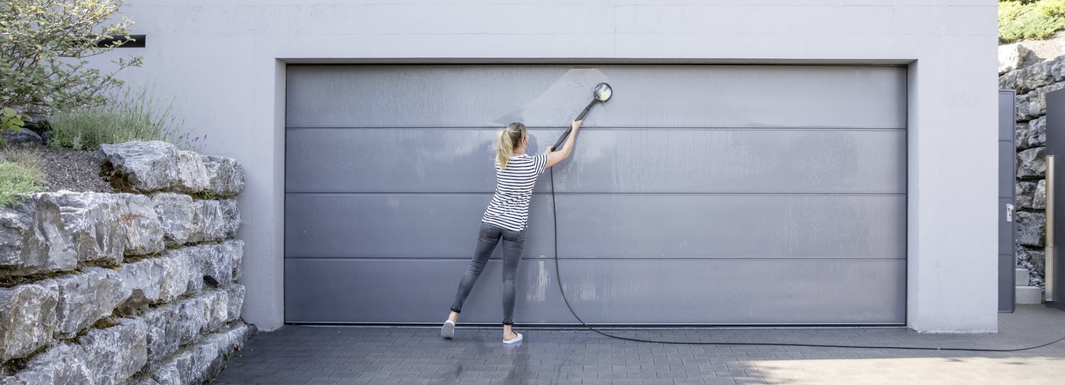 Nettoyer la porte de garage Une femme nettoie sa porte de garage avec une brosse de lavage Kärcher