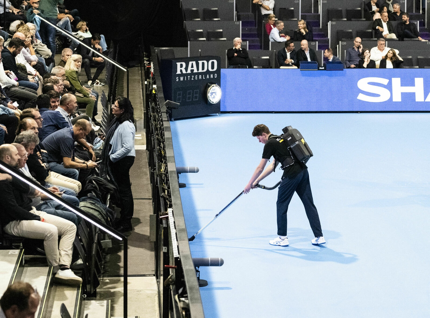Durch die Reinigung wird nicht nur für Sauberkeit, sondern auch für Sicherheit und Fairness im Spiel gesorgt. Foto von einem jungen Mann, der mit einem Rucksacksauger den Rand des Center-Courts reinigt: Durch die Reinigung wird nicht nur für Sauberkeit, sondern auch für Sicherheit und Fairness im Spiel gesorgt.