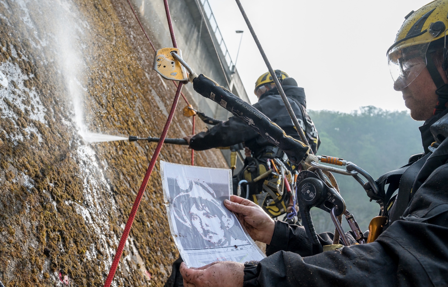 Kletterer bringen das Reverse Graffiti auf den Staudamm.