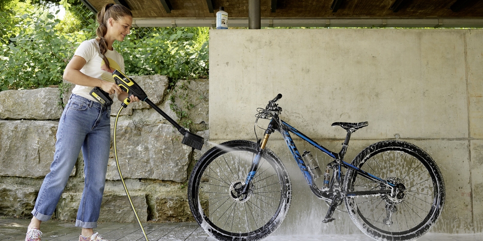 Une femme nettoie son vélo avec le nettoyeur haute pression sans fil Kärcher