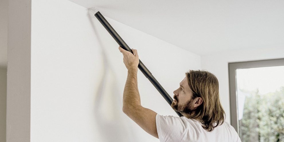 Un homme aspire le plafond de son logement à l’aide d’un flexible de rallonge