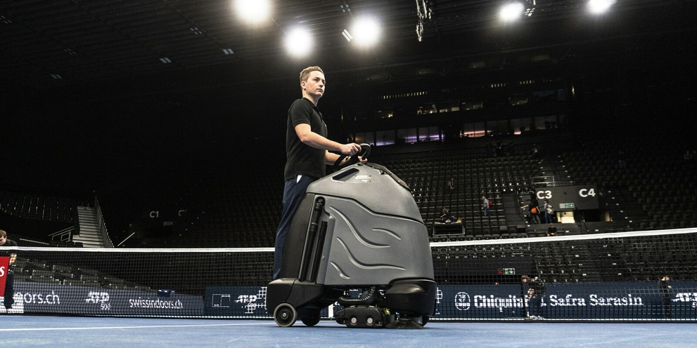 Schnell über den Center-Court flitzen, um die feinen Filzfasern zu beseitigen, die sich von den Tennisbällen lösen. Bild von Person auf Aufsteh-Scheuersaugmaschine: Schnell über den Center-Court flitzen, um die feinen Filzfasern zu beseitigen, die sich von den Tennisbällen lösen.