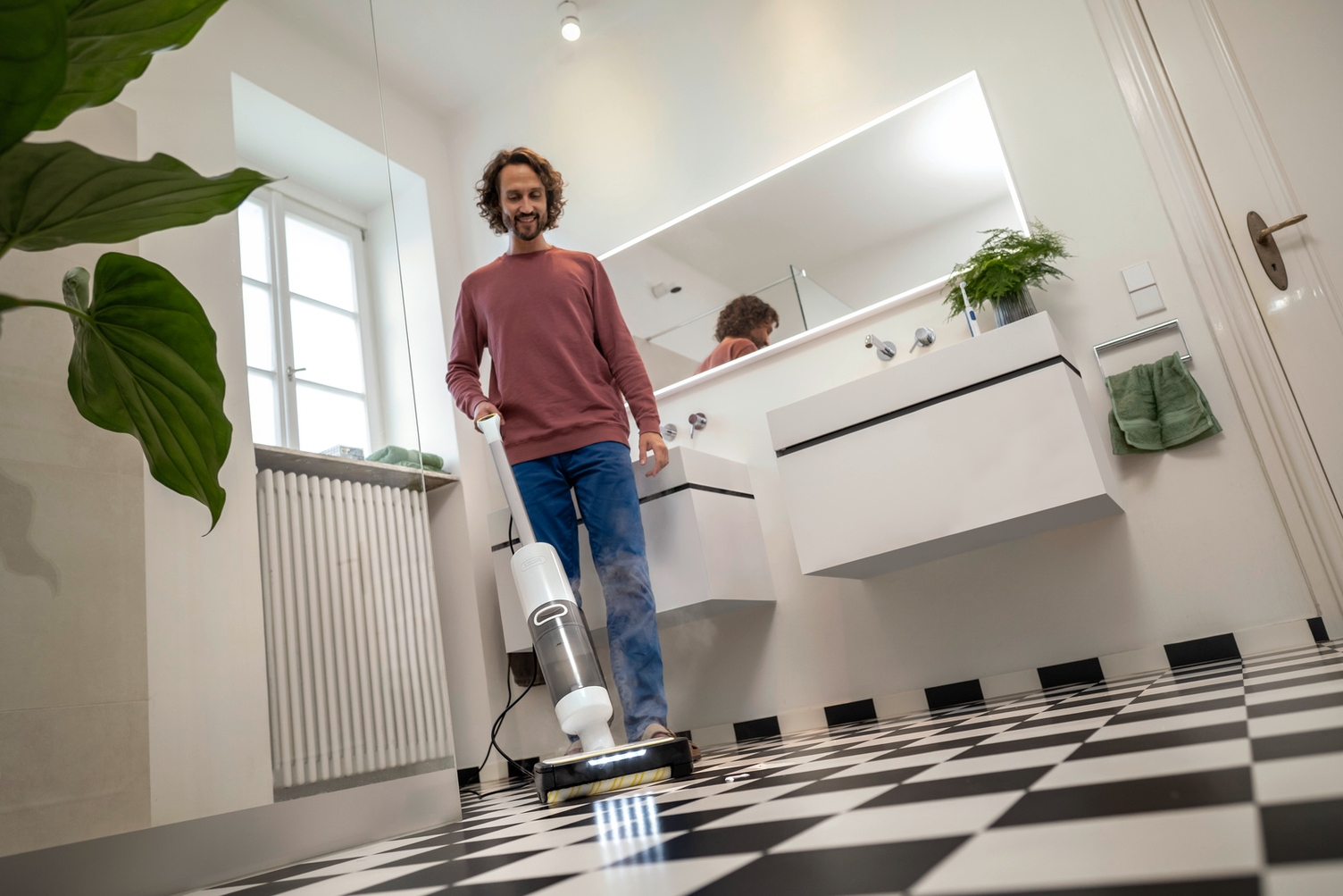 Ein Mann reinigt den gefliesten Boden eines modernen Badezimmers mit den Kärcher Dampfsauger SCV 4 Steam Vac.
