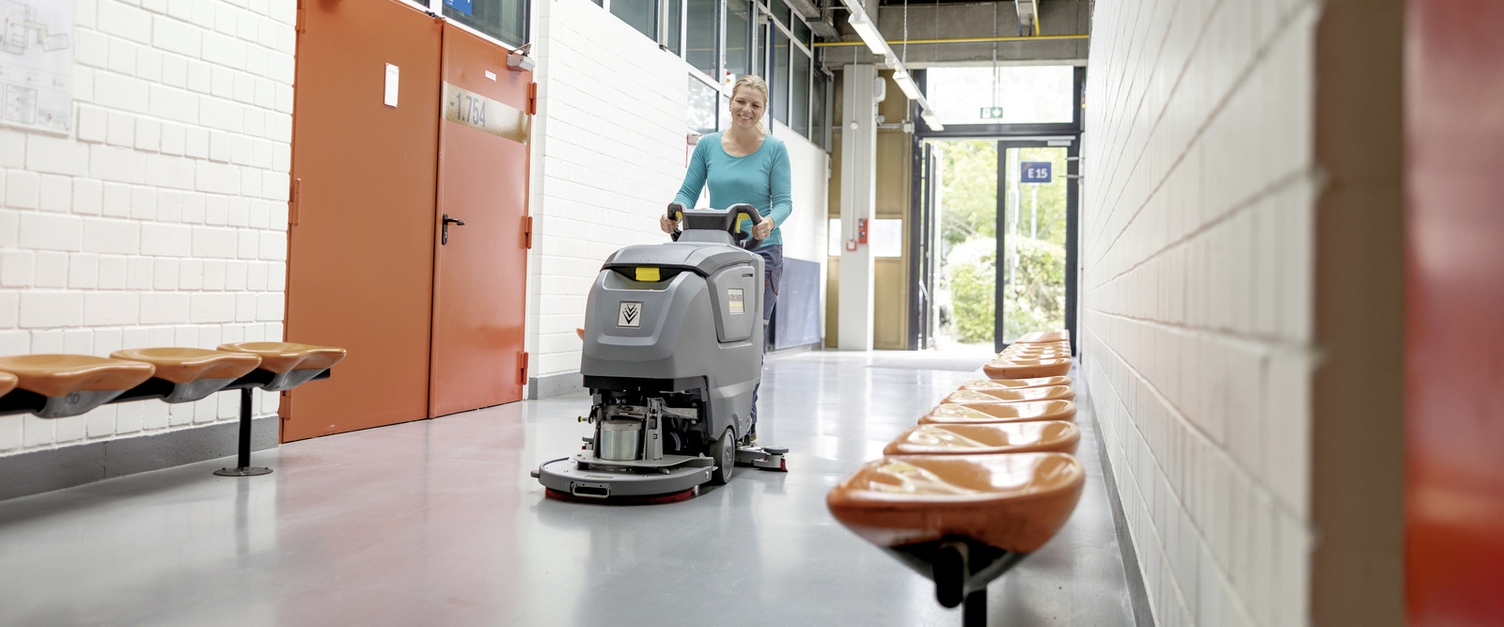 Eine Frau übernimmt die Innenreinigung im Flur mit einer handgeführten Scheuersaugmaschine