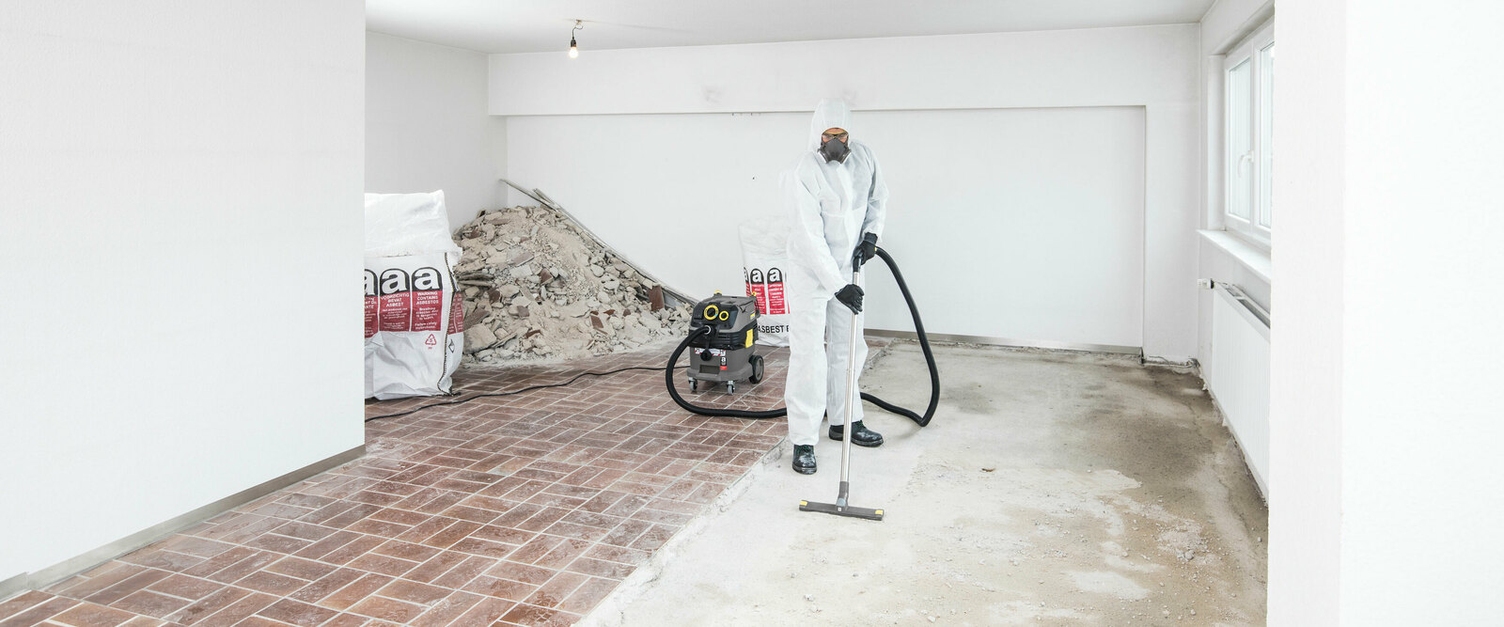 Asbest auf der Baustelle eine Person in weißer Schutzkleidung reinigt mit einem Kärcher Sauger Rückstände auf dem Boden einer sanierten Wohnung