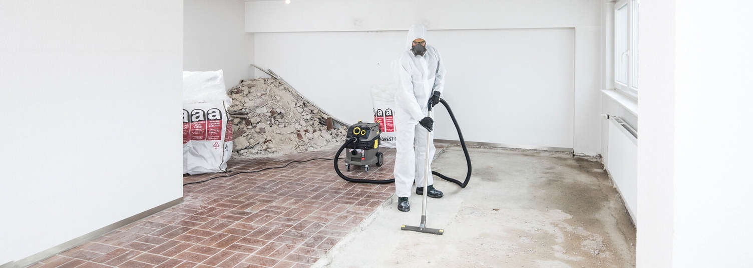 eine Person in weißer Schutzkleidung reinigt mit einem Kärcher Sauger Rückstände auf dem Boden einer sanierten Wohnung