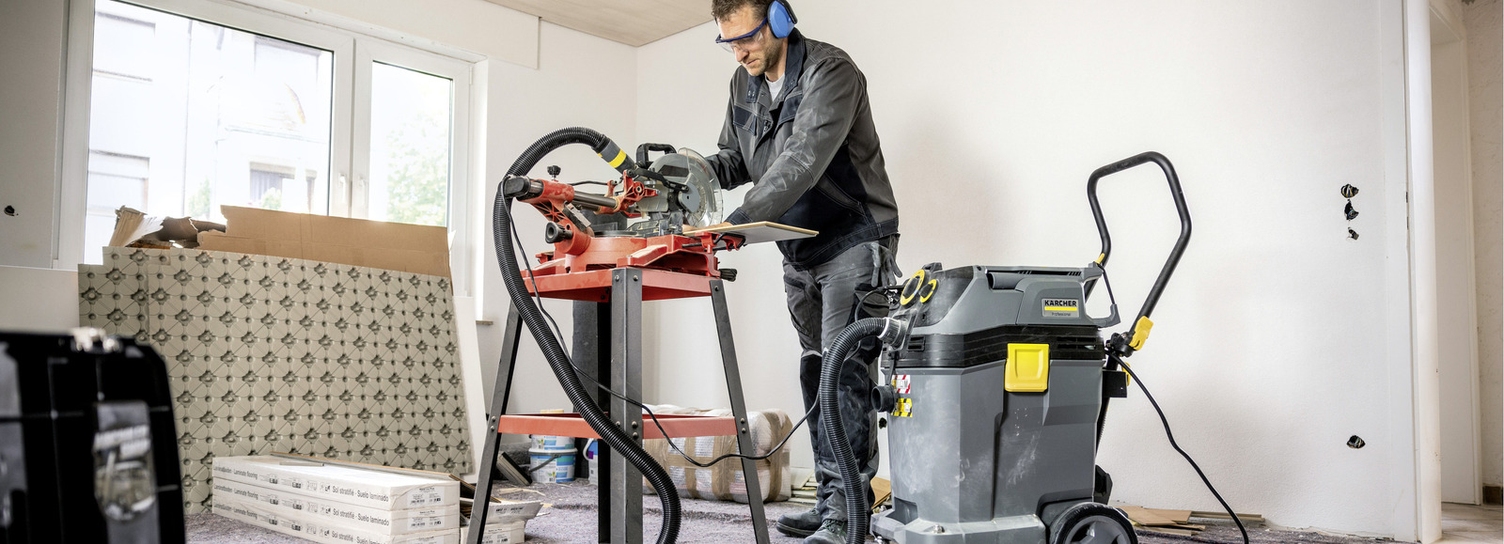 Eine Person reinigt mit einem Kärcher Sauger die Werkbank einer Maschine