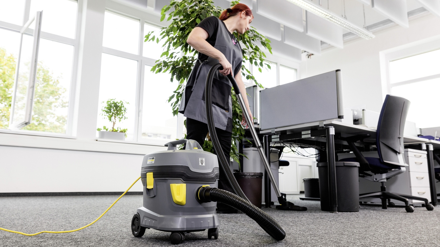 Eine Person reinigt mit einem Staubsauger von Kärcher einen Büroraum