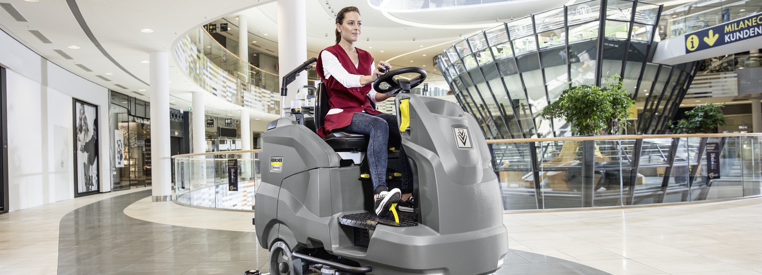 Eine Person reinigt den Boden eines Einkaufszentrums mithilfe einer Aufsitz-Kehrmaschine