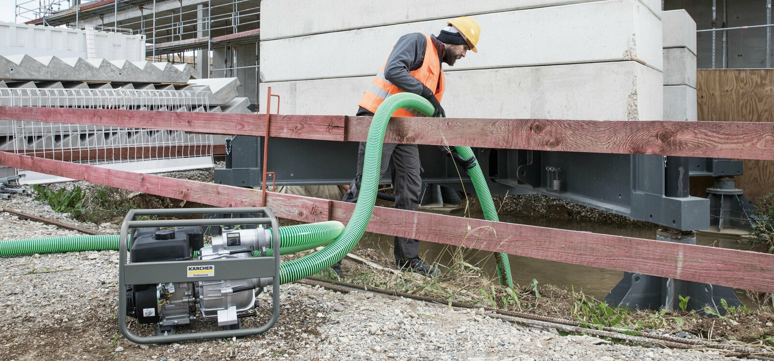 Eine Person saugt mit einem grünen Rohr und der Kärcher Schmutzwasserpumpe Schmutzwasser aus einem Baugraben