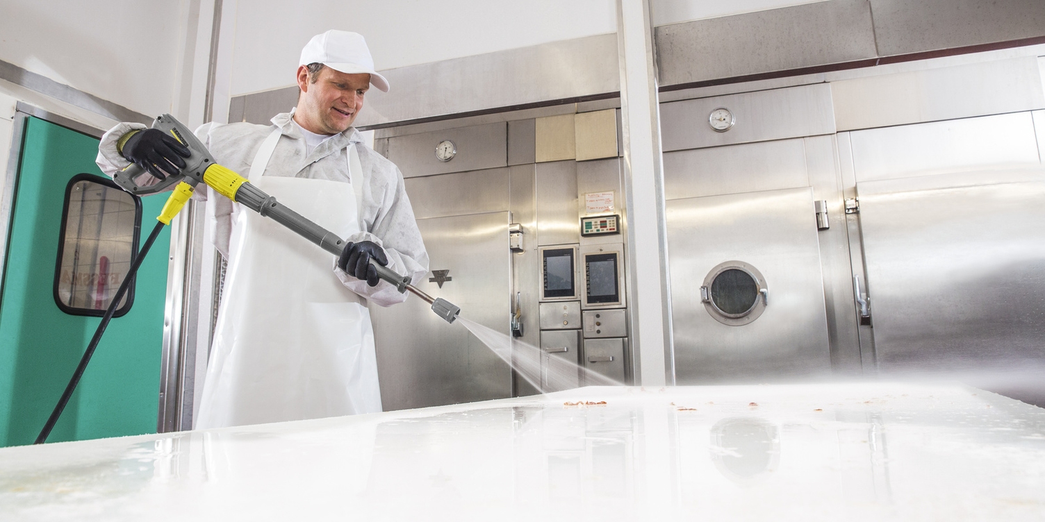 Ein Mann in weißer Arbeitskleidung reinigt mit einem Kärcher Hochdruckreiniger eine Arbeitsfläche