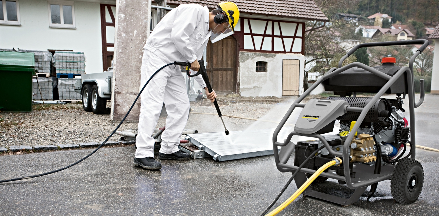 Gerüstreinigung mit Höchstdruck Eine Person in weißer Arbeitskleidung reinigt eine Gerüsttafel mit einem Kärcher Höchstdruckreiniger