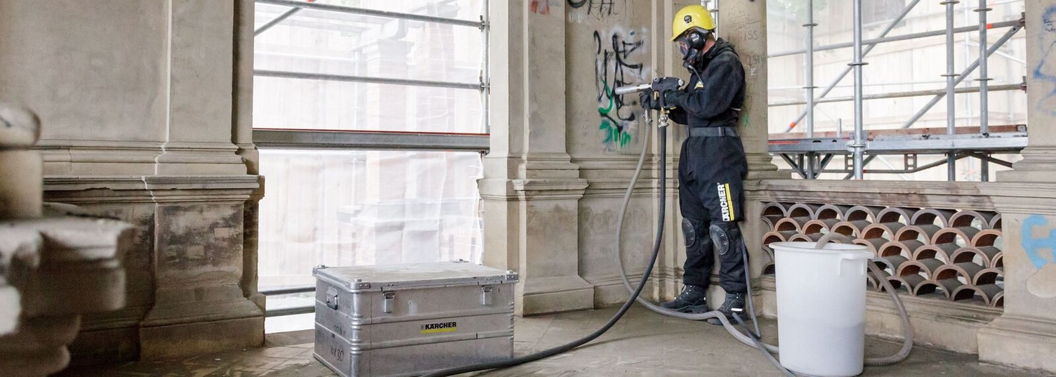 eine Person in Schutzkleidung entfernt Graffiti von der Innenseite einer Hauswand