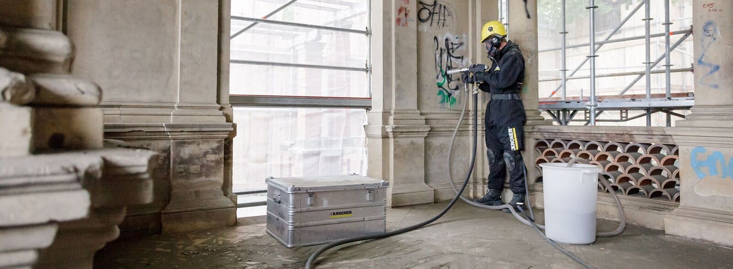 Eine Person entfernt mit einem Hochdruckreiniger Graffiti von einer Wand