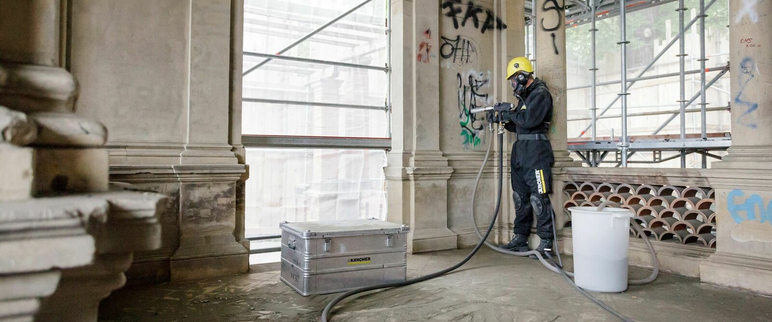 Eine Person in Schutzkleidung entfernt Graffiti von der Innenseite einer Hauswand