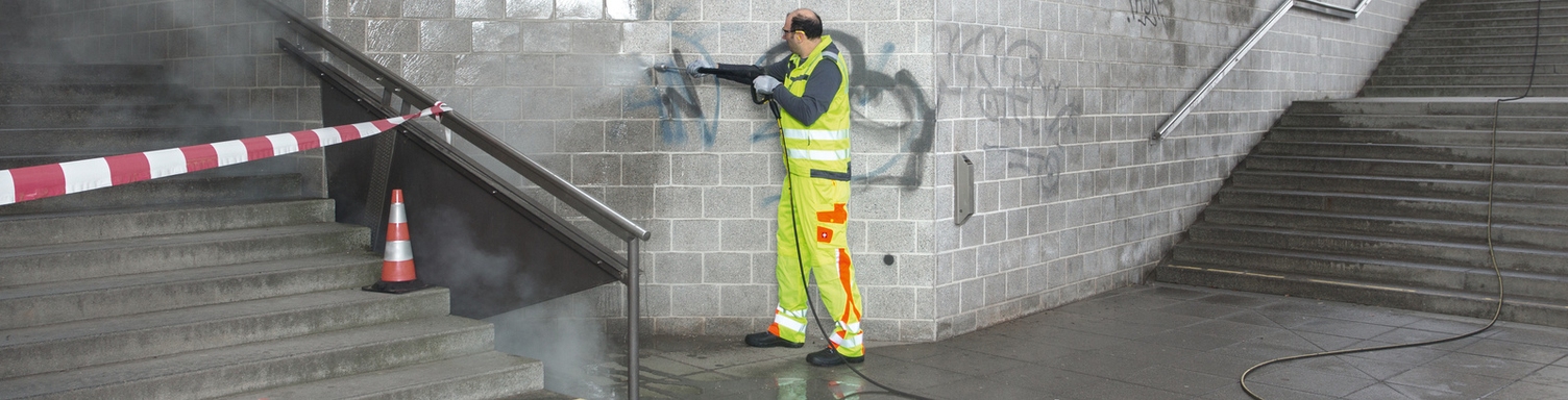 In einer Unterführung entfernt eine Person mit Hilfe eines Kärcher Hochdrucktrailers Graffiti