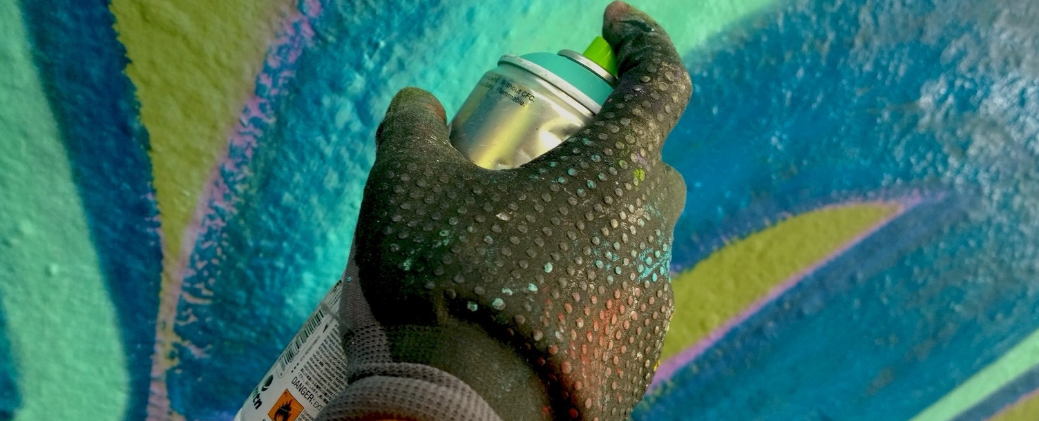 Eine Hand im Handschuh sprüht mit einer Graffitidose Farbe auf eine Wand