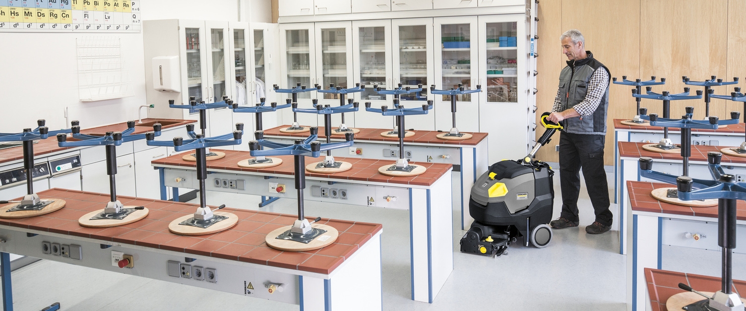 Eine Person bedient eine Scheuersaugmaschine im Klassenzimmer