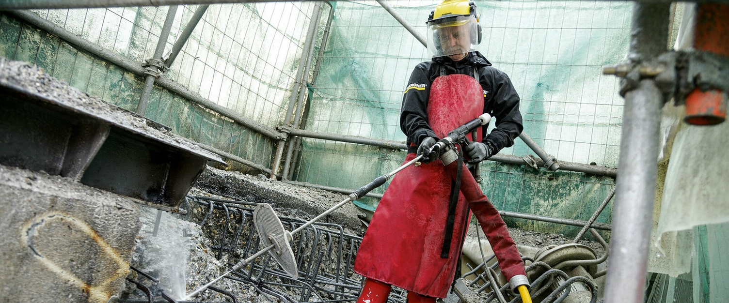 Betonsanierung mit Höchstdruckwasserstrahlen eine Person in Schutzkleidung nutzt einen Kärcher Höchstdruckreiniger zum Reinigen von Beton-Bauschutt