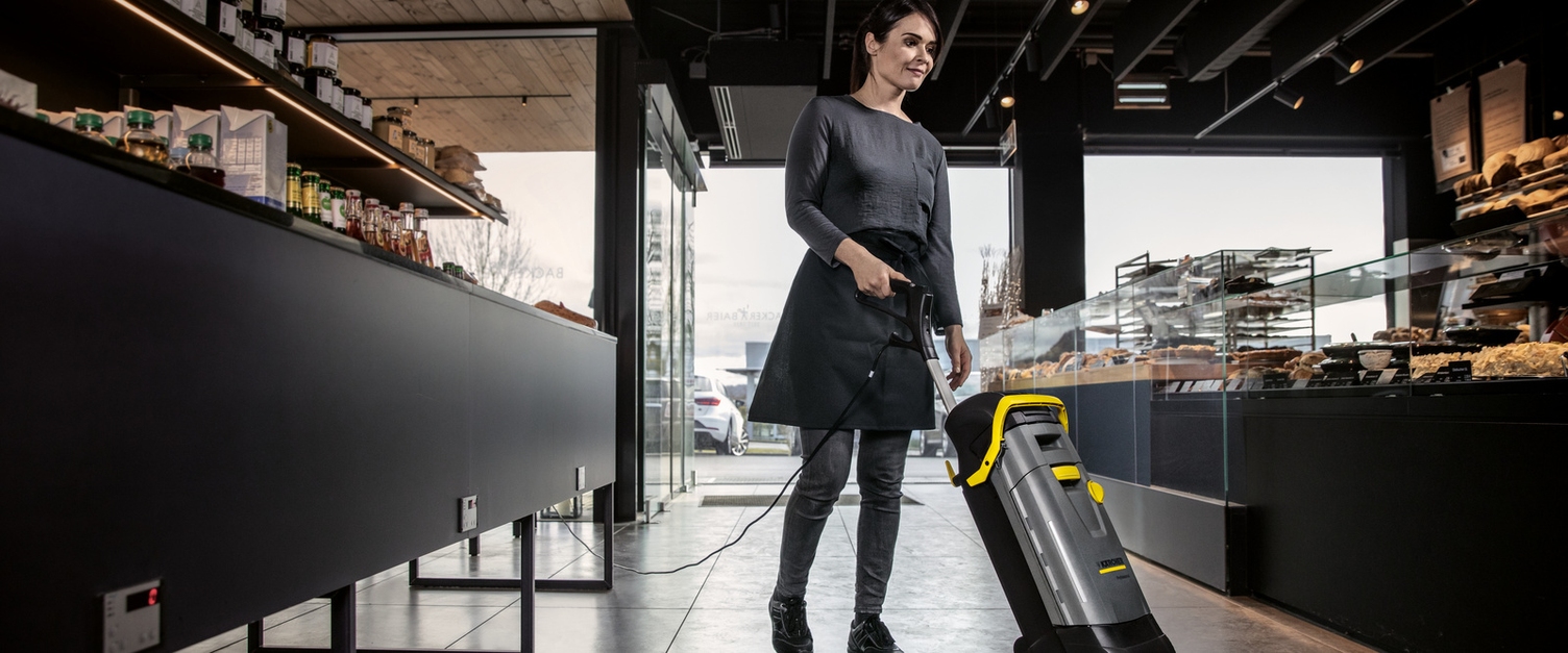 Reinigung in der Bäckerei Frau mit Staubsauger, die den Boden innerhalb einer Bäckerei reinigt.