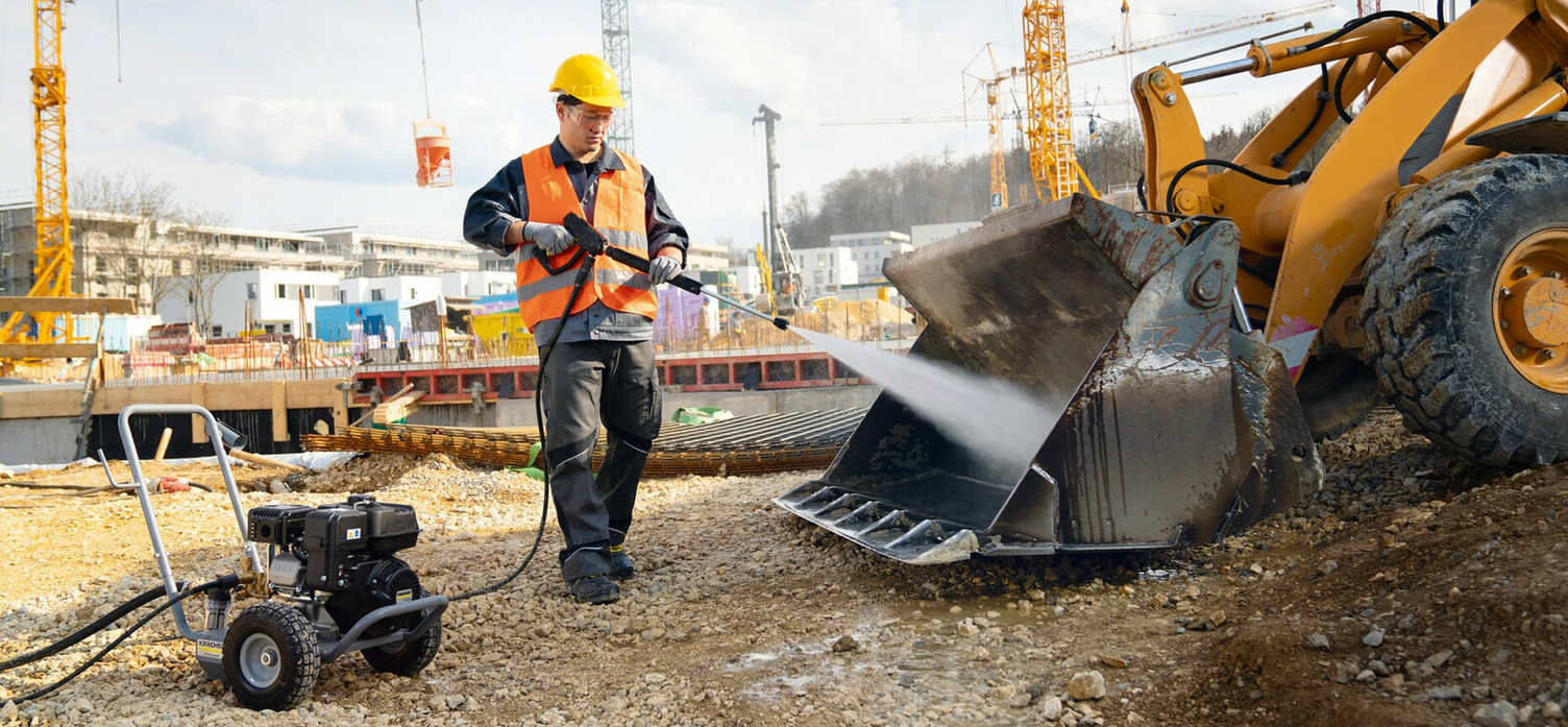 Eine Person reinigt mit einem Kärcher Hochdruckreiniger mit Verbrennungsmotor die Schaufel eines Baggers