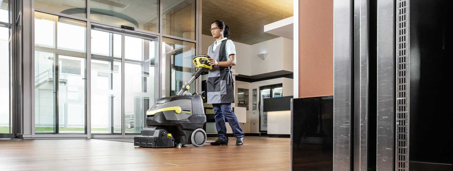 Eine Person bedient eine Scheuersaugmaschine von Kärcher auf Holzboden
