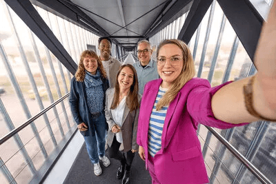 Fünf lächelnde Kärcher-Mitarbeiter posieren für ein Gruppen-Selfie auf einem modernen Büro-Laufsteg aus Glas und Stahl