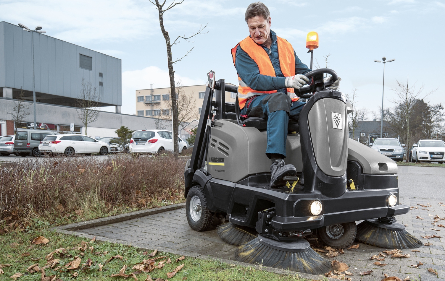 Eine Person säubert mit einer Kehrmaschine einen Parkplatz