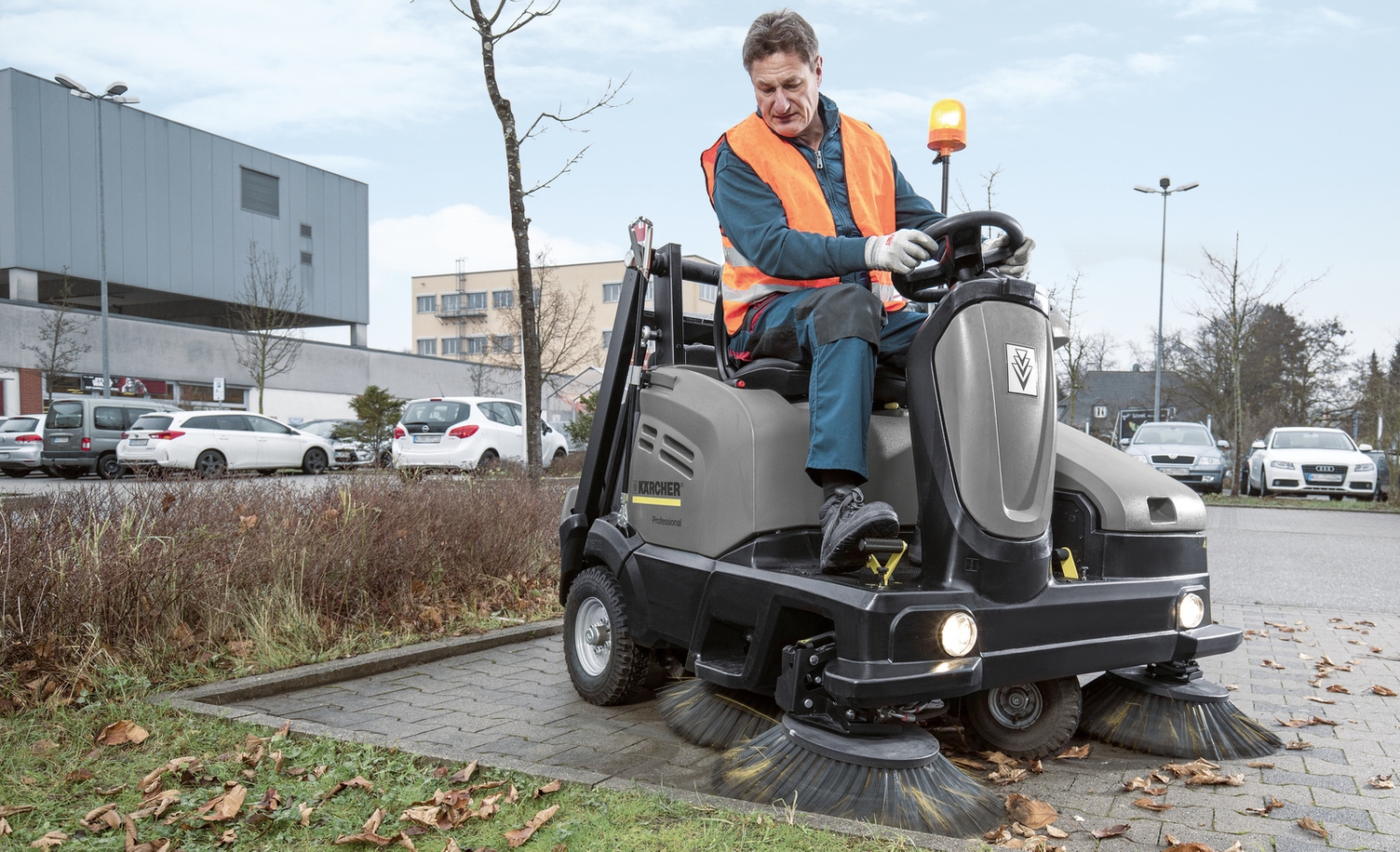 Eine Person sitzt auf einer Kehrmaschine und reinigt einen Parkplatz