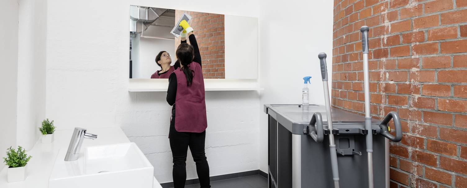 Eine Person reinigt den Spiegel im Toilettenbereich