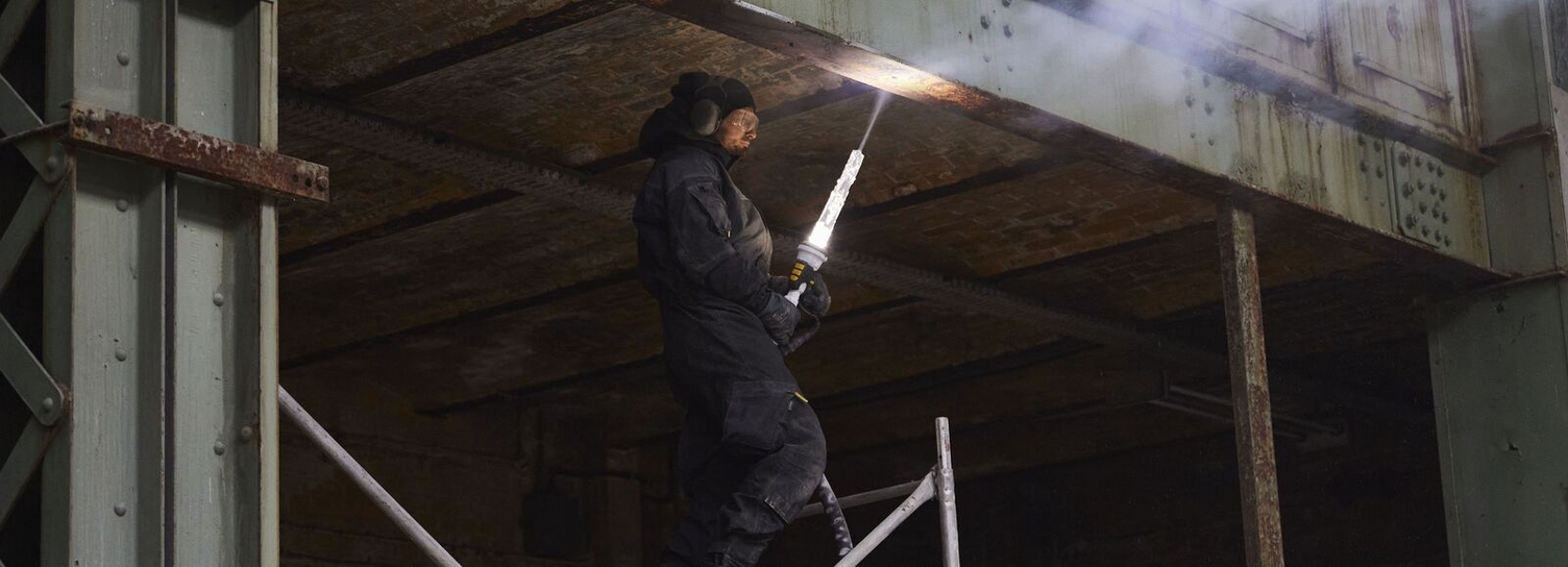 Eine Person reinigt einen Metallbalken mit Trockeneis