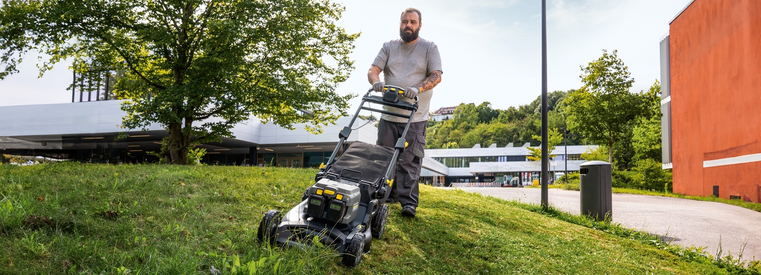 Ein Mann mäht mit einem Rasenmäher eine Grünfläche