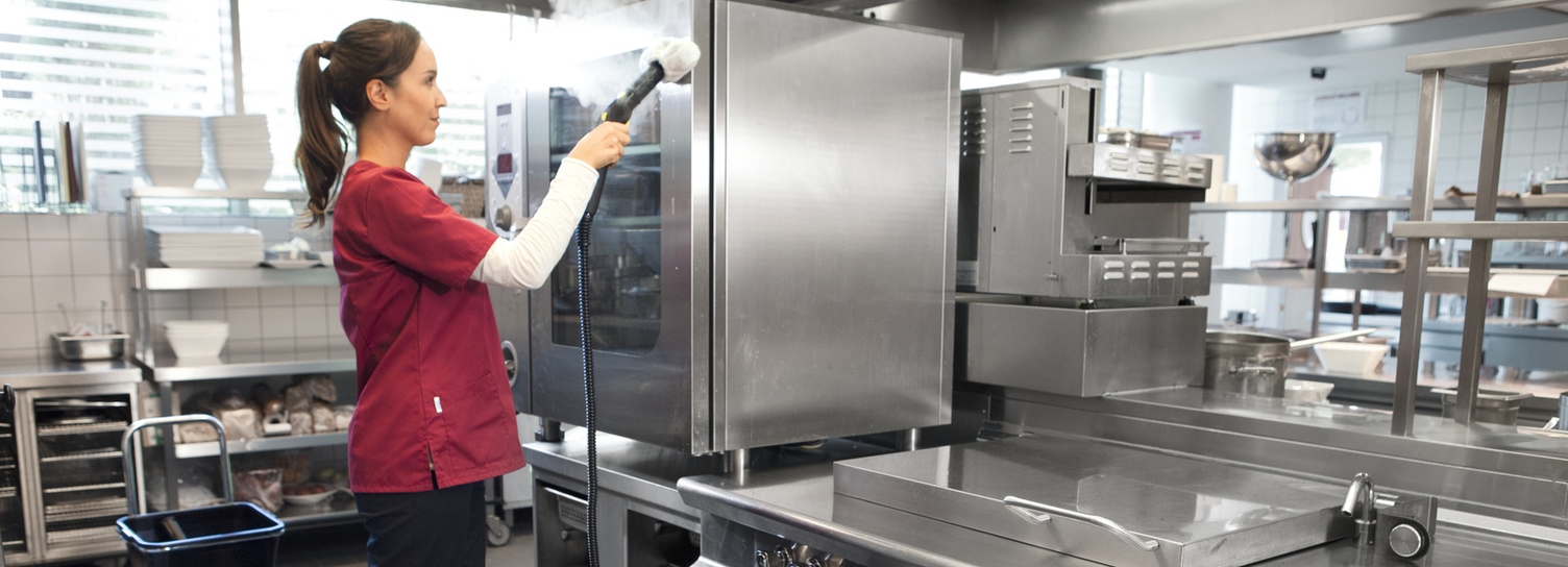 Eine Frau säubert mit einem Dampfreiniger die Fläche eines Küchenschrankes