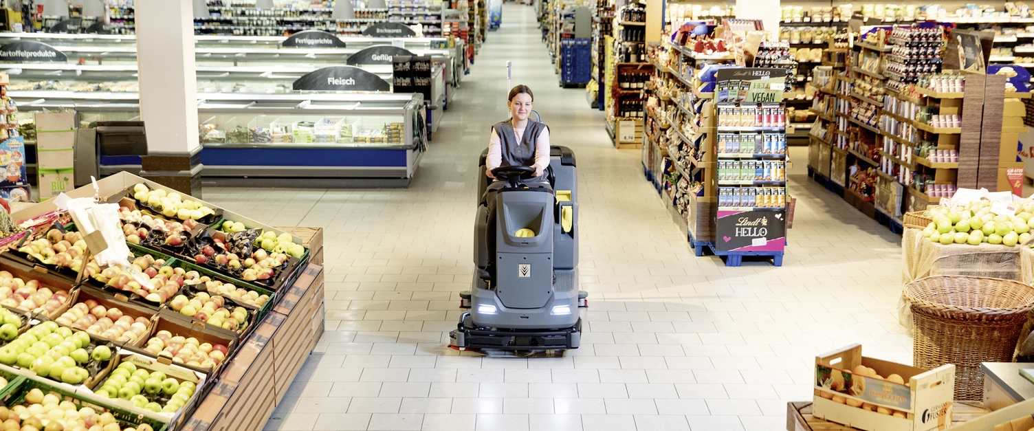 Eine Person sitzt auf einer Scheuersaugmaschine und reinigt ein Lebensmittelgeschäft