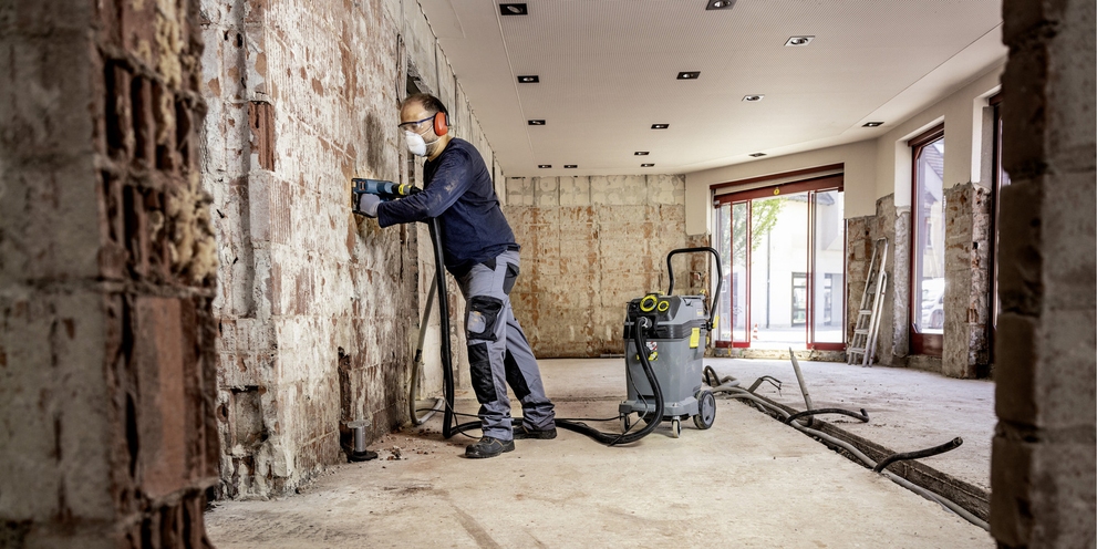 ein Mann in Bauuniform reinigt eine Wand im Rohbau mit einem Sicherheitssauger