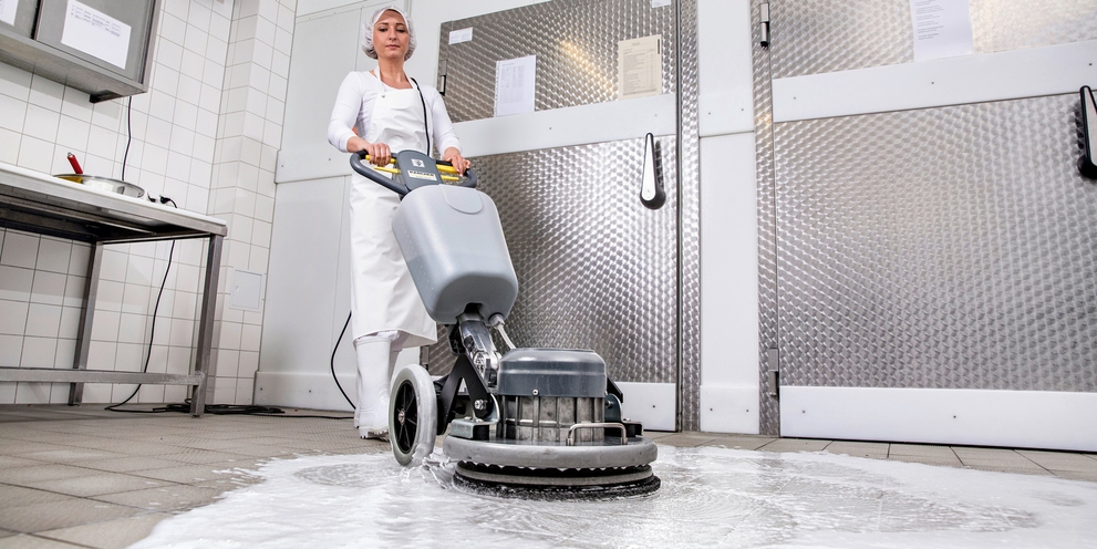 Ein Frau in weißer Arbeitskleidung reinigt mit einer Kärcher Eischeibenmaschine den Boden einer Metzgerei