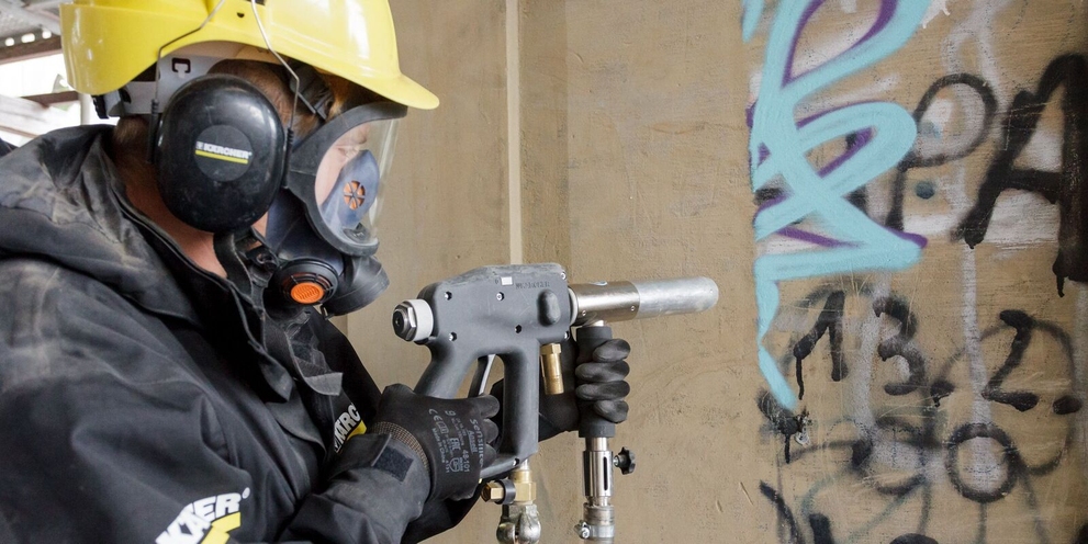 Eine Person entfernt ein Graffiti von einer Steinmauer