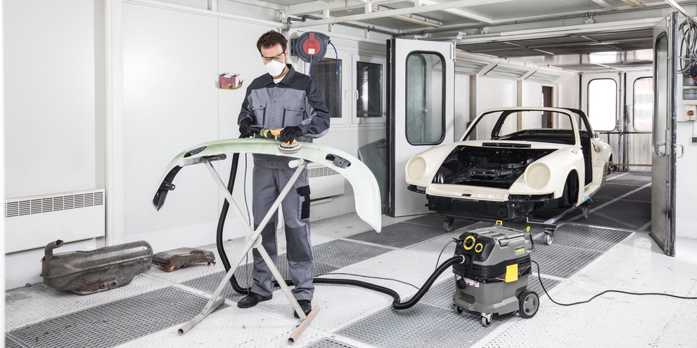 Ein Mann saugt in einer Lackierkabine den Staub während seines Arbeitsprozesses ab