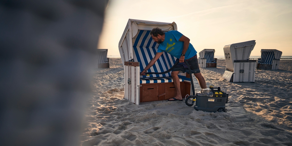 Ein Mann reinigt am Strand einen Strandkorb mit einem Kärcher Puzzi 9/1 Bp Ein Mann reinigt am Strand einen Strandkorb mit einem Kärcher Puzzi 9/1 Bp