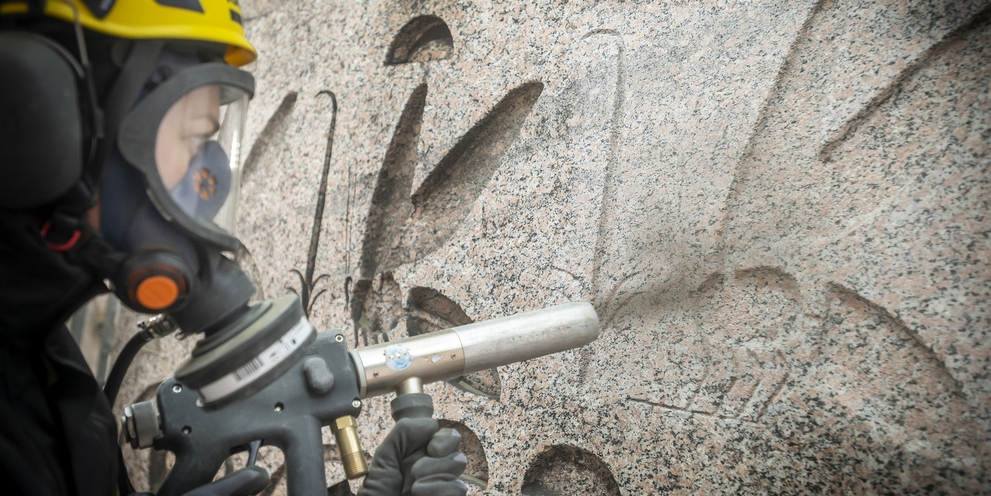 Eine Person in Schutzausrüstung reinigt ein Denkmal mit Kärcher Strahlpistole