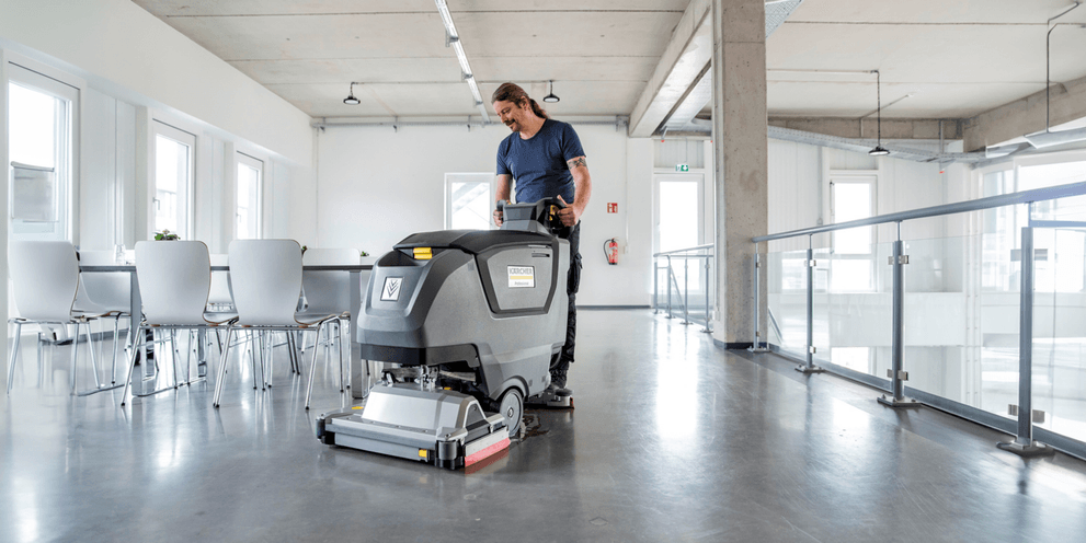 Mann sitzt auf Scheuersaugmaschine und poliert Boden.