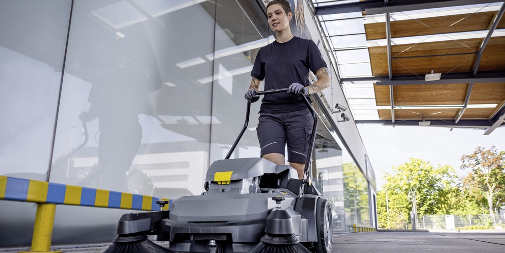 Eine Person reinigt einen Außenbereich mit einer Kehrmaschine von Kärcher